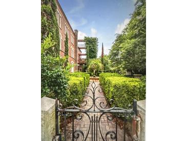 View of the garden through a black wrought iron gate and leading to a brick building with greenery at 309 Meeting St # 19, Charleston, SC 29401