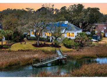 Charming waterfront home featuring a private dock, lush landscaping, and a serene setting at sunset at 12 Trachelle Ln, Charleston, SC 29407