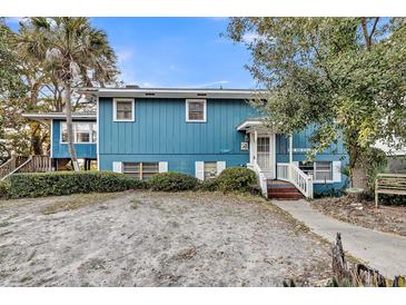 Charming blue two-story home with a well-manicured lawn and a welcoming front porch and mature landscaping at 702 E Erie Ave, Folly Beach, SC 29439