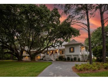 Charming exterior featuring a sprawling lawn, mature trees, and a classic white facade, all complemented by a scenic sunset backdrop at 1456 Mcpherson Lndg, Johns Island, SC 29455