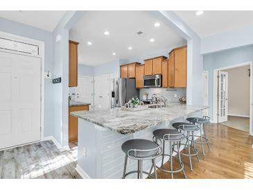 A view of kitchen island with seating and a light blue backsplash with light brown cabinetry and stainless steel appliances at 102 Harbor Point Ct, Summerville, SC 29486