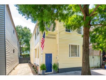Charming yellow home featuring a blue door and an American flag, nestled under lush green trees at 21 America St, Charleston, SC 29403