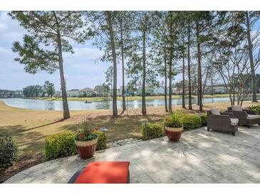A tranquil backyard patio overlooks a serene lake, framed by mature trees and lush landscaping at 415 Four Seasons Blvd, Summerville, SC 29486