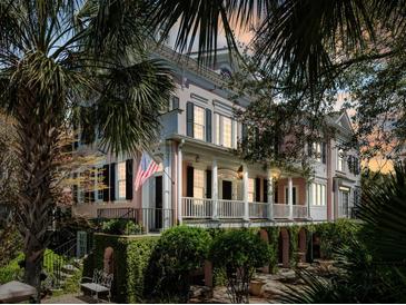Elegant two-story house featuring a porch with white columns surrounded by lush landscaping and mature palm trees at 14 Greenhill St, Charleston, SC 29401