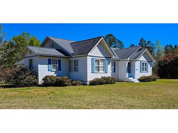 Charming white home featuring a gray roof and vibrant blue shutters, surrounded by lush landscaping at 8524 Cane Branch Rd, Ruffin, SC 29475