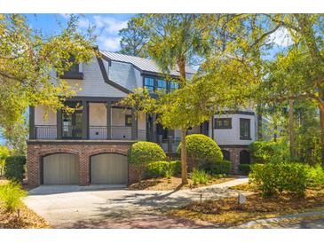 Charming two-story home featuring a brick façade, metal roof, second story porch, and manicured landscaping at 3121 Marshgate Dr, Johns Island, SC 29455