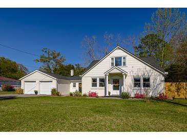 Charming home featuring white siding, a black roof, manicured lawn and a detached two car garage at 418 Geddes Ave, Charleston, SC 29407