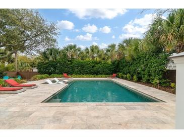 Inviting backyard pool with lounge chairs and a stone patio surrounded by palm trees and lush greenery at 3405 Cameron Blvd, Isle of Palms, SC 29451
