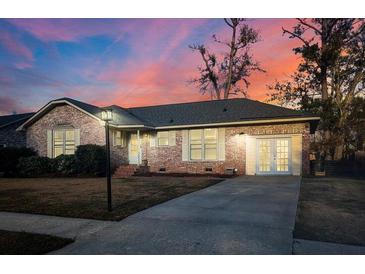 Charming brick home featuring a driveway, well-manicured lawn, and classic architectural details against a colorful sunset sky at 135 Tall Pines Rd, Ladson, SC 29456