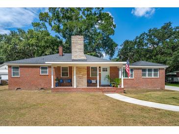 Charming brick home featuring a welcoming front porch, lush landscaping, and a classic American flag at 1756 Mchenry Ave, Charleston, SC 29412
