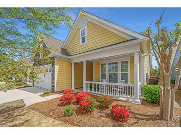 Charming yellow home with a stone garage, inviting front porch and vibrant landscaping at 2010 Redback Dr, Summerville, SC 29483