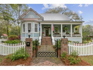 Charming light blue two-story home with a landscaped yard, brick gate posts, and a quaint white picket fence at 803 S Main St, Summerville, SC 29483