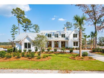 Beautiful white home with a metal roof and professionally landscaped front yard and mature trees at 116 Peninsula Dr, Ravenel, SC 29470