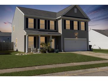 Charming two-story home with a well-manicured lawn and inviting front porch at dusk at 243 Donatella Dr, Goose Creek, SC 29445
