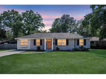 Charming brick home with a lush green lawn and inviting front porch with an orange colored front door at 733 Longfellow Rd, Charleston, SC 29407