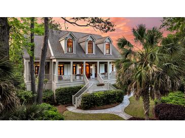 Charming two-story home with inviting front porch, landscaped yard, mature palm trees, and colorful sunset backdrop at 2104 Royal Pine Dr, Seabrook Island, SC 29455
