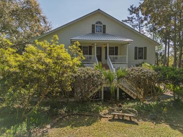 Charming two-story home with a metal roof, inviting front porch and lush landscaping at 8551 Pope Landing Rd, Edisto Island, SC 29438