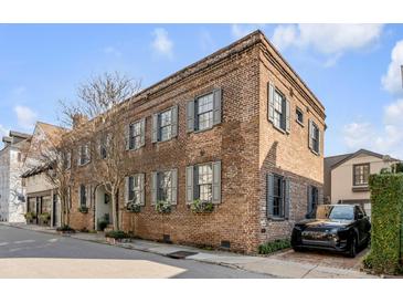 Stunning red brick exterior with gray shutters, a black car parked on the side, and lush landscaping at 70 King St, Charleston, SC 29401