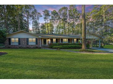 Charming brick home boasts a well-manicured lawn and mature trees at sunset at 112 Furlong Rd, Summerville, SC 29483