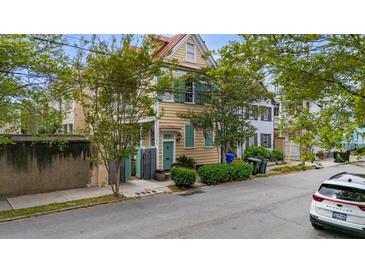 Charming two-story home with a light yellow exterior, teal shutters and door, and mature trees at 197 Coming St, Charleston, SC 29403