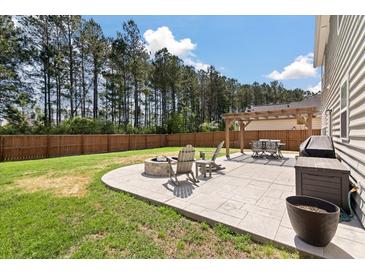 Landscaped backyard with a stone patio, fire pit, dining pergola, and wooded perimeter for privacy at 210 Witch Hazel St, Summerville, SC 29486