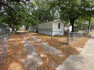 Exterior view of a mobile home featuring a gated drive and mature shade trees at 5626 Shelton St, North Charleston, SC 29406