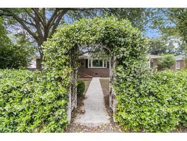 Charming brick home featuring a flower-covered archway, walkway, and manicured green hedges at 1023 Shelley Rd, Charleston, SC 29407