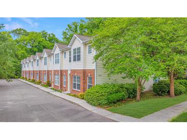 Townhome with cream siding and red brick bottom, surrounded by lush trees and landscaping at 241 Howle Ave # H, Charleston, SC 29412