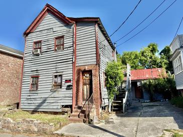Two-story home featuring deteriorating wood siding and a small, overgrown yard needing repair at 6 Moultrie St, Charleston, SC 29403