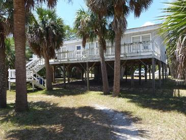 Charming coastal home elevated with a spacious deck, perfect for enjoying the surrounding palm trees and ocean breeze at 2604 Palmetto Blvd, Edisto Island, SC 29438