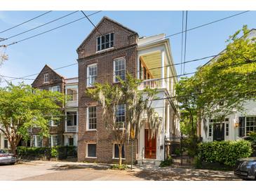 Charming brick and white two-story house with a balcony and lush trees on a sunny day at 17 Wentworth St, Charleston, SC 29401