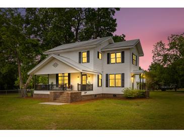 Charming two-story home with a covered porch, large yard, and warm lighting at twilight at 285 Roosevelt Dr, Saint Stephen, SC 29479