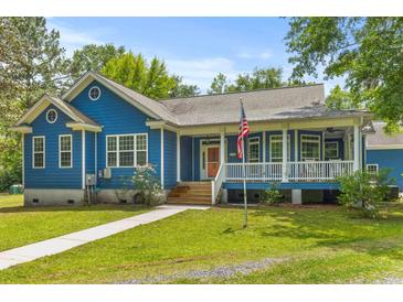 Charming blue home features a covered porch and an American flag displayed in the landscaped front yard at 6035 Bay Pond Rd, Ravenel, SC 29470