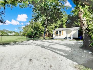 Charming home featuring a light yellow exterior, green trees, and a spacious gravel area at 1915 Quitman St, North Charleston, SC 29405