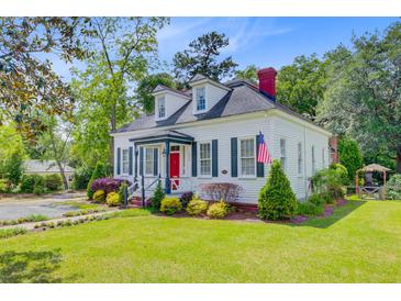 Charming white home with a red door, green shutters, dormer windows, and manicured landscaping at 318 N Magnolia St, Summerville, SC 29483