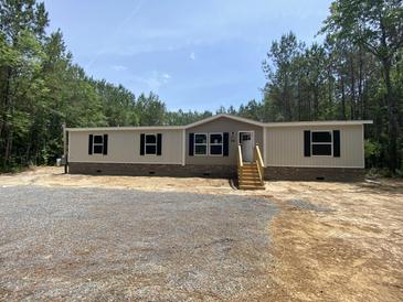 New manufactured home with tan and grey siding, black shutters, wood porch steps, and gravel in the front yard at 852 Lawyer Ln, Cross, SC 29436