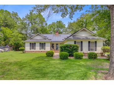 Charming ranch-style home featuring a lush green lawn, mature trees, and solar panels on the roof at 4 Garth Dr, Charleston, SC 29414