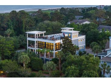 Beautiful multi-story home with multiple balconies and rooftop deck, surrounded by lush greenery at dusk at 2213 Rolling Dune Rd, Seabrook Island, SC 29455