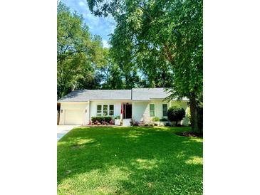Charming white brick home featuring an attached garage, mature trees, and a well-manicured lawn at 1015 Jacksnipe Ln, Mount Pleasant, SC 29464
