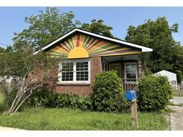 Charming brick home with colorful sunburst design above the porch, surrounded by lush greenery and a blue mailbox at 2204 Dover St, North Charleston, SC 29405