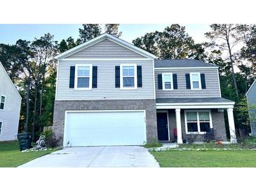 Two-story home featuring a two-car garage, gray brick accents, black shutters, and well-maintained landscaping at 619 Red Mulberry Rd, Moncks Corner, SC 29461