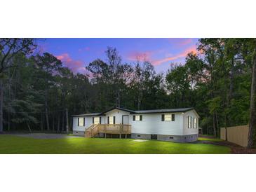 Charming single-story home with a wooden deck, surrounded by a lush lawn and serene forest backdrop at twilight at 117 Dairy Ln, Cottageville, SC 29435