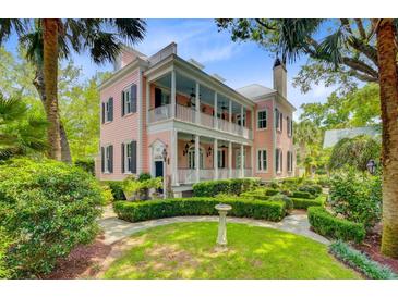 Charming two-story pink home featuring double balconies, a manicured lawn and a lush garden at 62 Eastlake Rd, Mount Pleasant, SC 29464