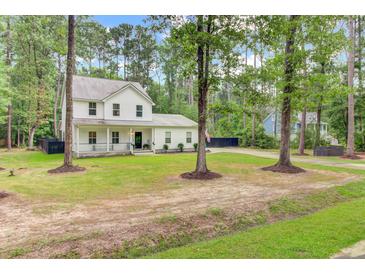 Charming two-story home with a welcoming front porch and lush green lawn surrounded by mature trees at 6190 Button Bush Dr, Ravenel, SC 29470