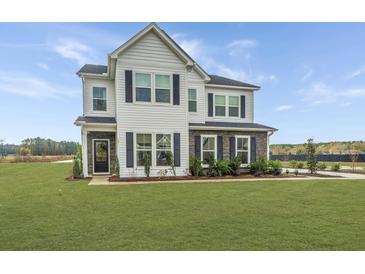 Beautiful two-story home showcasing a well-manicured lawn, stone accents, and black shutters under a bright blue sky at 111 Augusta Pass Dr, Ridgeville, SC 29472