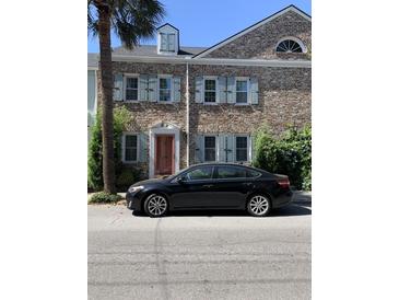 Charming brick townhouse featuring light blue shutters, decorative windows, and a neatly landscaped yard at 128 Queen St, Charleston, SC 29401