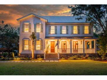 Stunning two-story home with a metal roof, large front porch and manicured lawn at sunset at 108 Live Oak Dr, Mount Pleasant, SC 29464