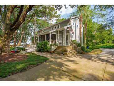 Charming gray home with inviting front porch, American flag, mature trees, and beautifully landscaped front yard at 2217 Ramsay St, Charleston, SC 29412