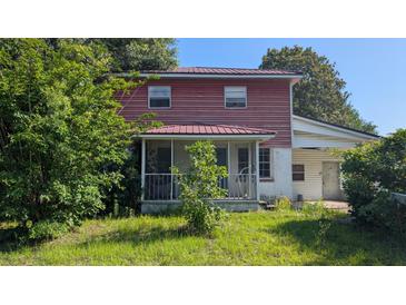 Two-story home with a screened-in porch, red siding, and a metal roof partially obscured by vegetation at 116 Stillfield Dr, Moncks Corner, SC 29461