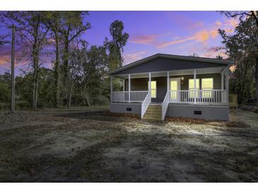 Charming single-story home featuring a covered porch, grey siding, and a well-maintained yard under a vibrant evening sky at 108 Wisteria Falls Ln, Saint Stephen, SC 29479